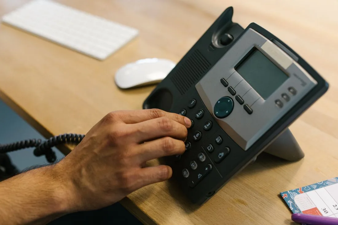 Dłoń wybierająca numer telefonu na biurku z klawiaturą i terminarzem w biurze